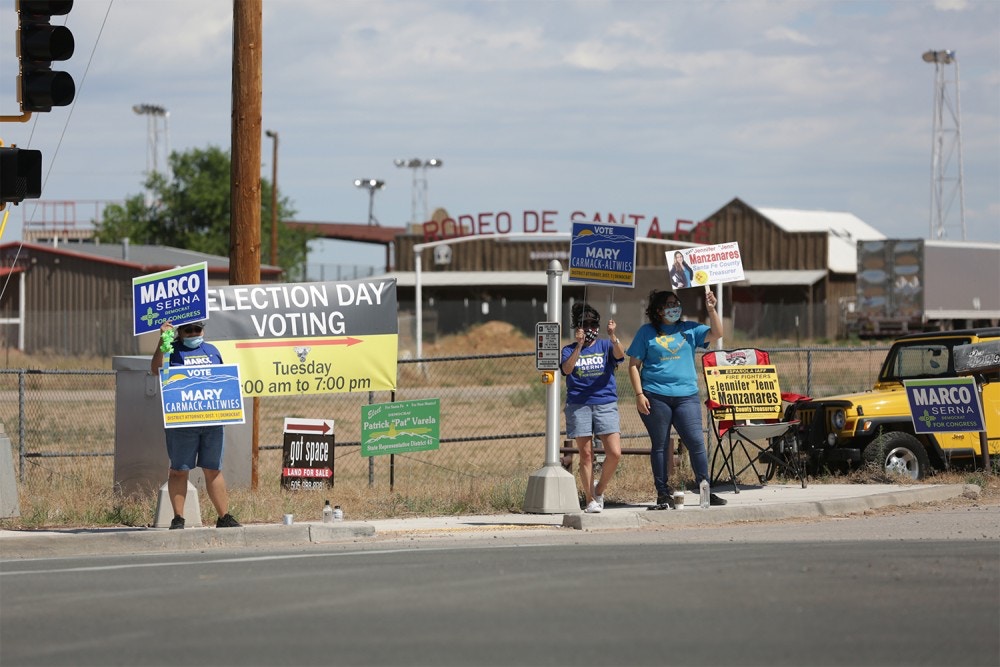 Campaigners wave signs for local and statewide Democratic candidates outside a polling place on Tuesday, June 2, 2020, in Santa Fe, New Mexico. Primaries for Democratic and Republican primary contests were held in New Mexico for the first time since the COVID-19 pandemic took hold. Poll workers wore surgical masks to prevent the spread of the virus and voters were given a squirt of hand sanitizer as they entered the building, a warehouse next to the county's rodeo grounds. (AP Photo/Cedar Attanasio)