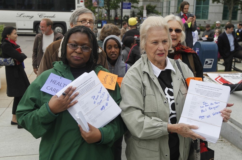 Rev. Yvonne McJetters, left, and Sarah Huffman carry copies of a petition with 4,000 signatures to Speaker Thom Tillis and President Pro Tem Phil Berger's offices at the North Carolina General Assembly building in Raleigh, N.C.  on Monday, April 23, 2012. A coalition of political watchdog groups gathered for the second "Rein Them In" rally prior to the noon start of a special legislative session. The petition calls on Tillis and Berger to oppose the enactment of a government-photo ID requirement and other legislation that will make it more difficult for registered voters to cast their ballots. (AP Photo/The News & Observer, Shawn Rocco)