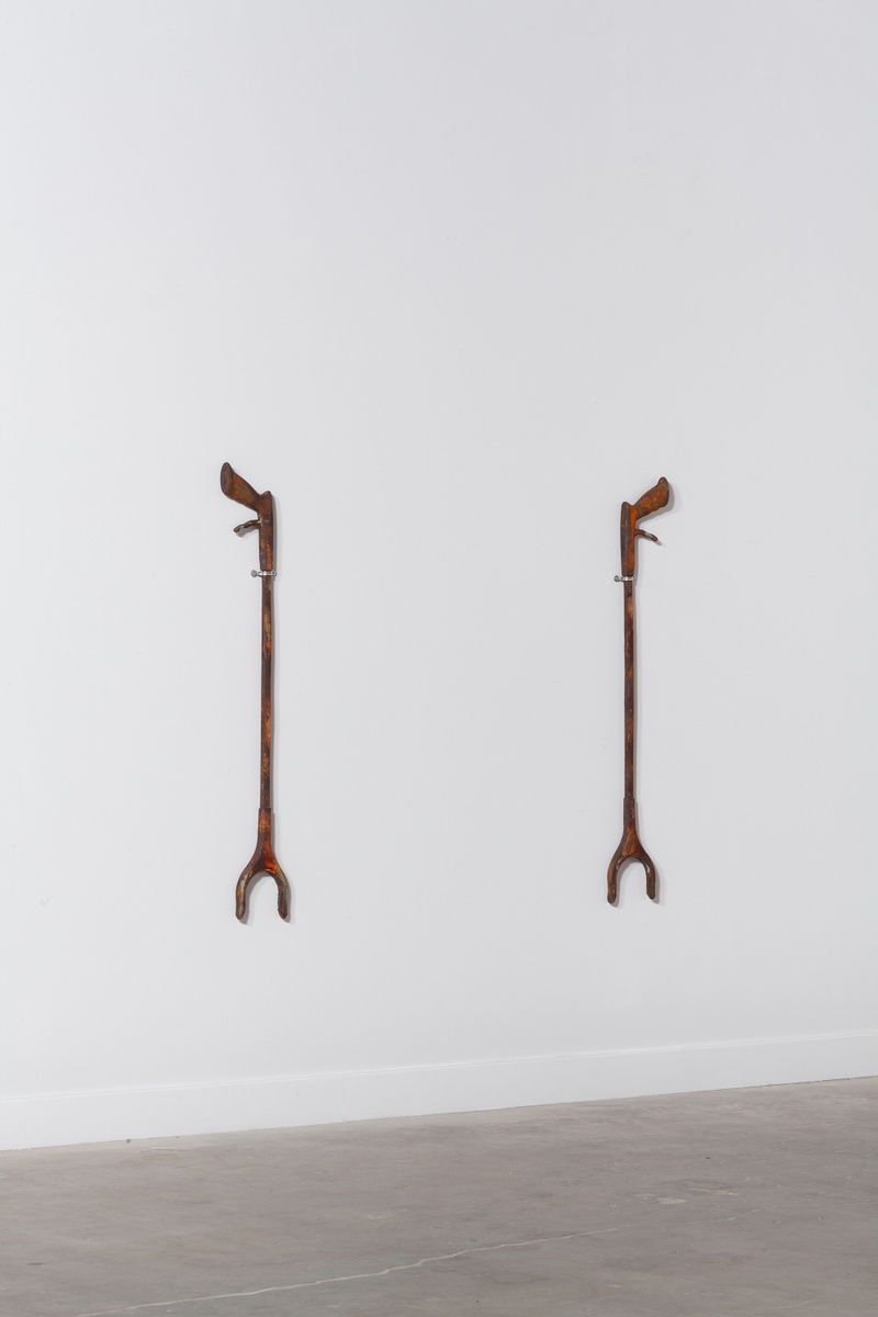 Hanging on a white wall are two large grabbers, similar to ones that Emily uses. The grabbers have a rusted hue.