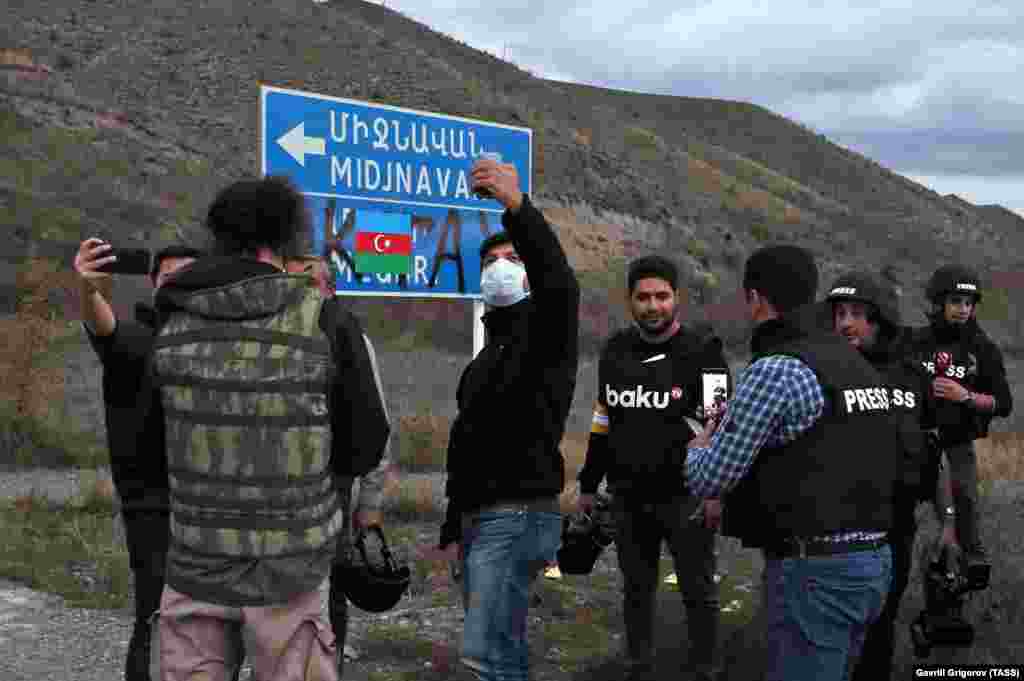 Journalists take selfies next to a defaced sign in territory recaptured by Azerbaijani forces on November 8.