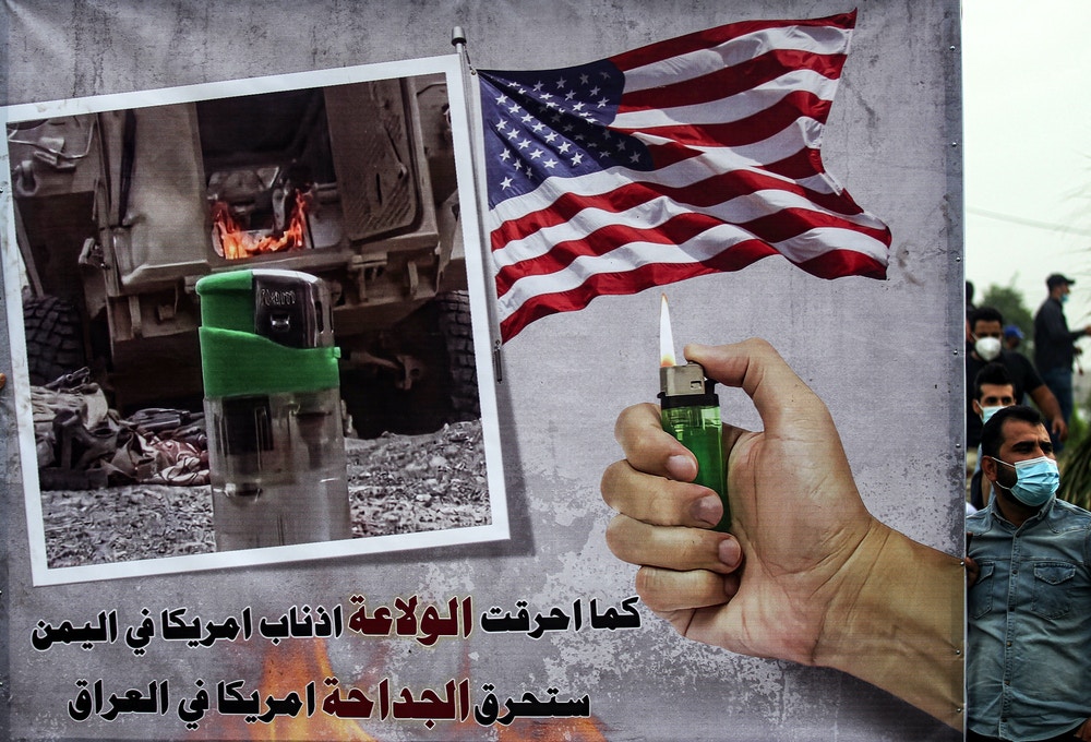 A sign depicting a hand holding a lighter beneath a US flag and next to a photo of a lighter near a military armoured vehicle with text reading in Arabic "as the lighter burned the followers of America in Yemen, the lighter will burn America in Iraq" is seen during a demonstration by supporters of the Iran-backed Hashed al-Shaabi (Popular Mobilisation) paramilitary forces outside the entrance to the Iraqi capital Baghdad's highly-fortified Green Zone on November 7, 2020, demanding the departure of remaining US forces from Iraq. - Several hundred protesters gathered in the Iraqi capital on Saturday afternoon to demand US troops leave the country in accordance with a parliament vote earlier this year. (Photo by Ahmad AL-RUBAYE / AFP) (Photo by AHMAD AL-RUBAYE/AFP via Getty Images)