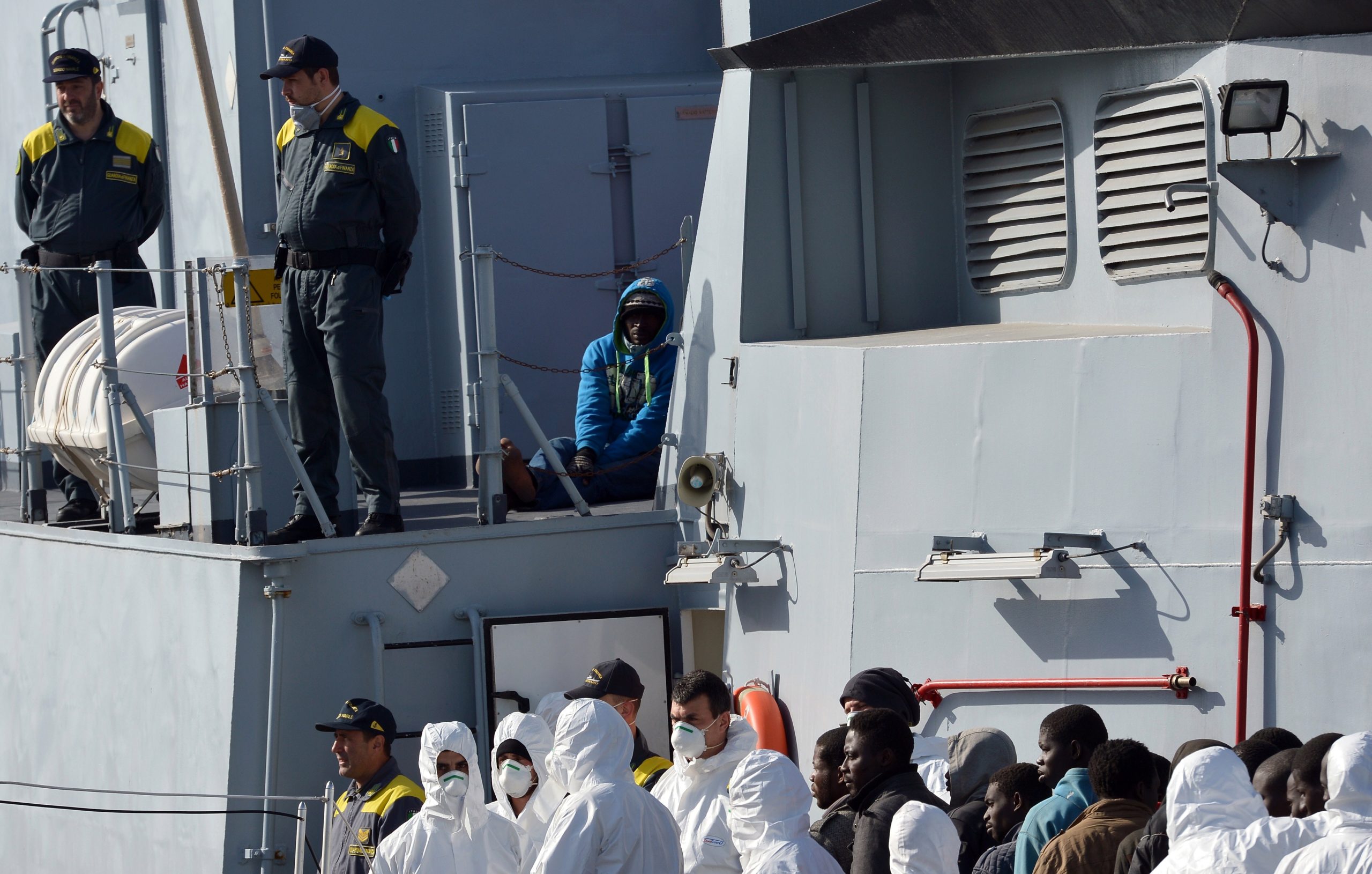 Italian police stand next to a migrant suspected to be a smuggler (up-R) as they disembark off rescued migrants from the Italian Guardia di Finanza vessel Denaro at the Sicilian harbour of Catania on April 23, 2015.